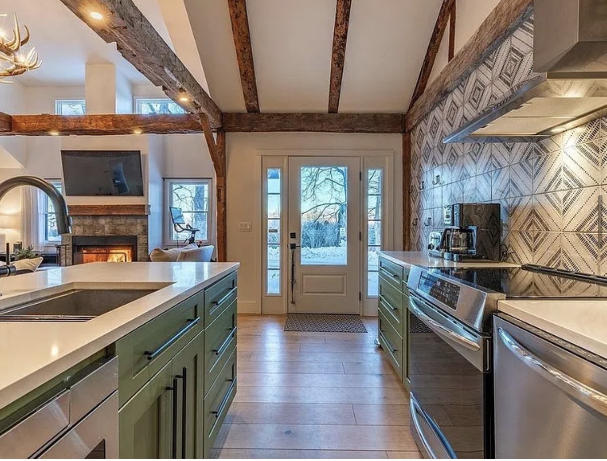 Kitchen with green cabinetry, exposed wood beams, and patterned tile backsplash