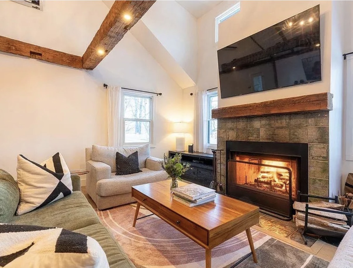 Living room with stone fireplace, vaulted ceiling, and wood beams