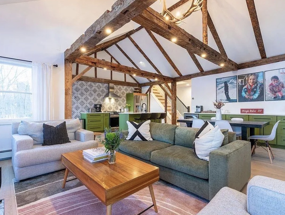 Open living space with green sofas, wood beams, and antler chandelier
