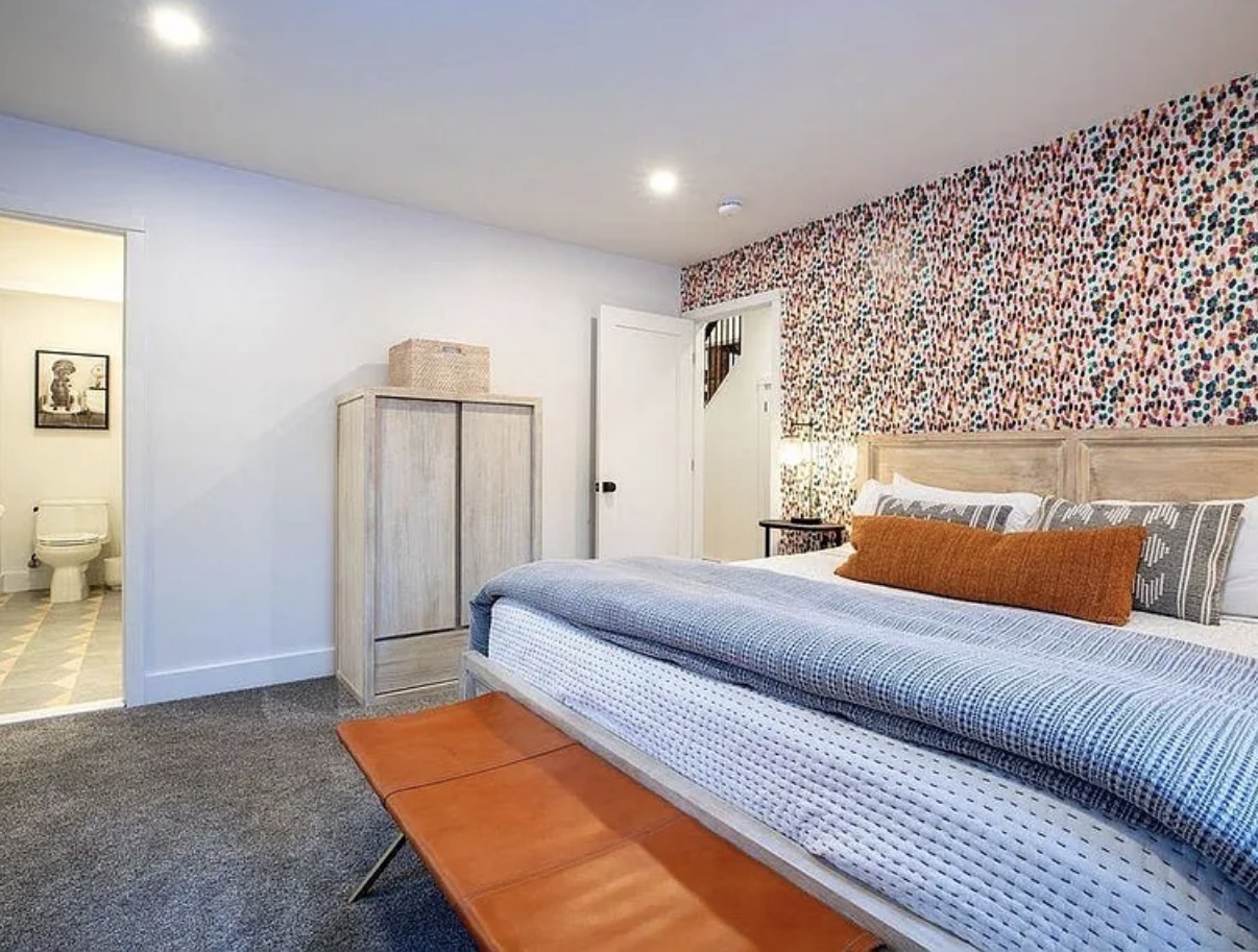 Primary bedroom with patterned wallpaper and leather bench