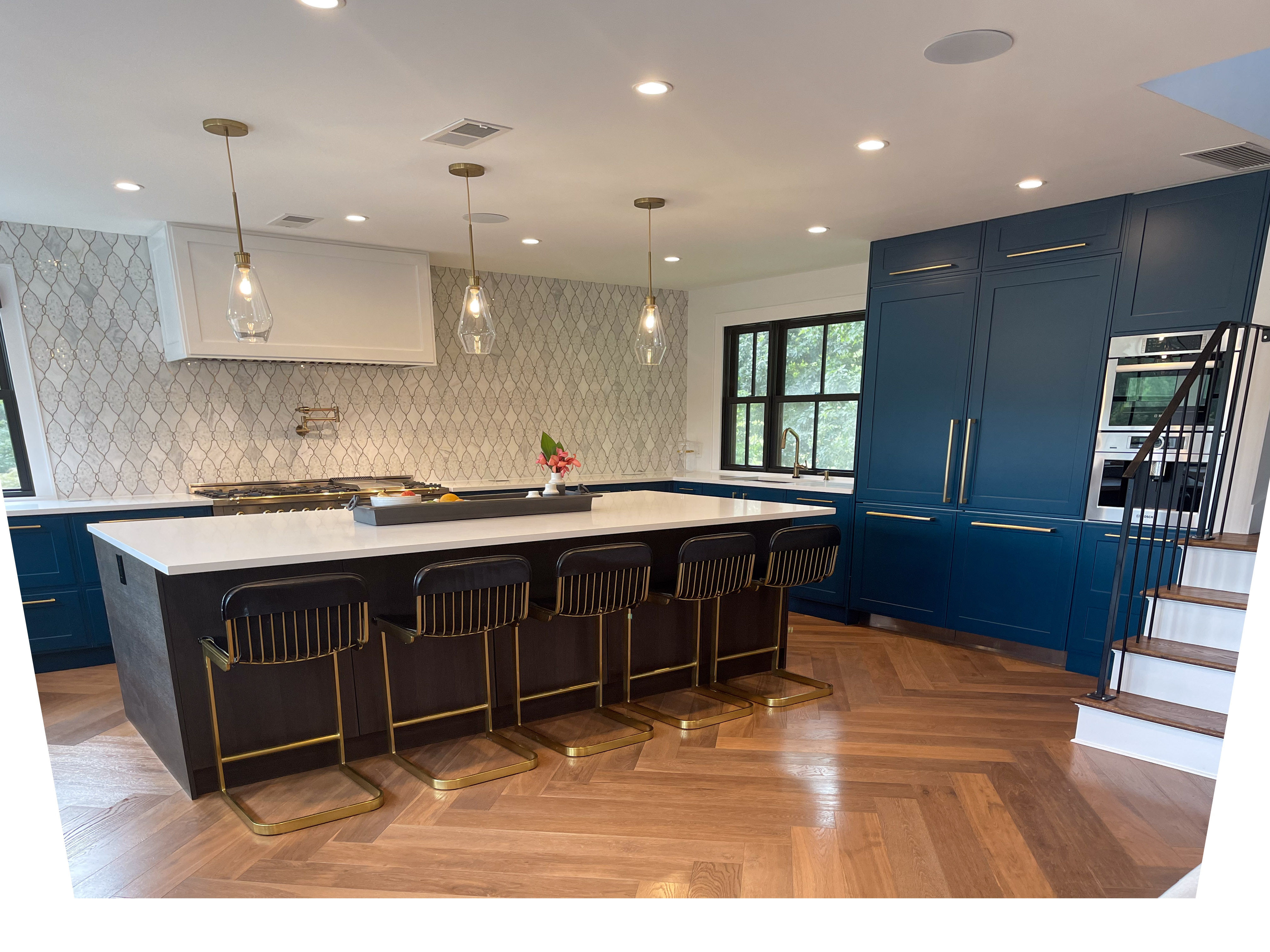 Navy blue kitchen with brass hardware, marble backsplash, and herringbone wood floors