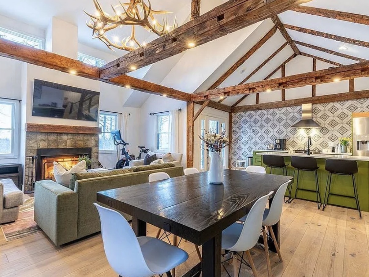 Vaulted living and dining space with exposed wood beams, antler chandelier, and open kitchen